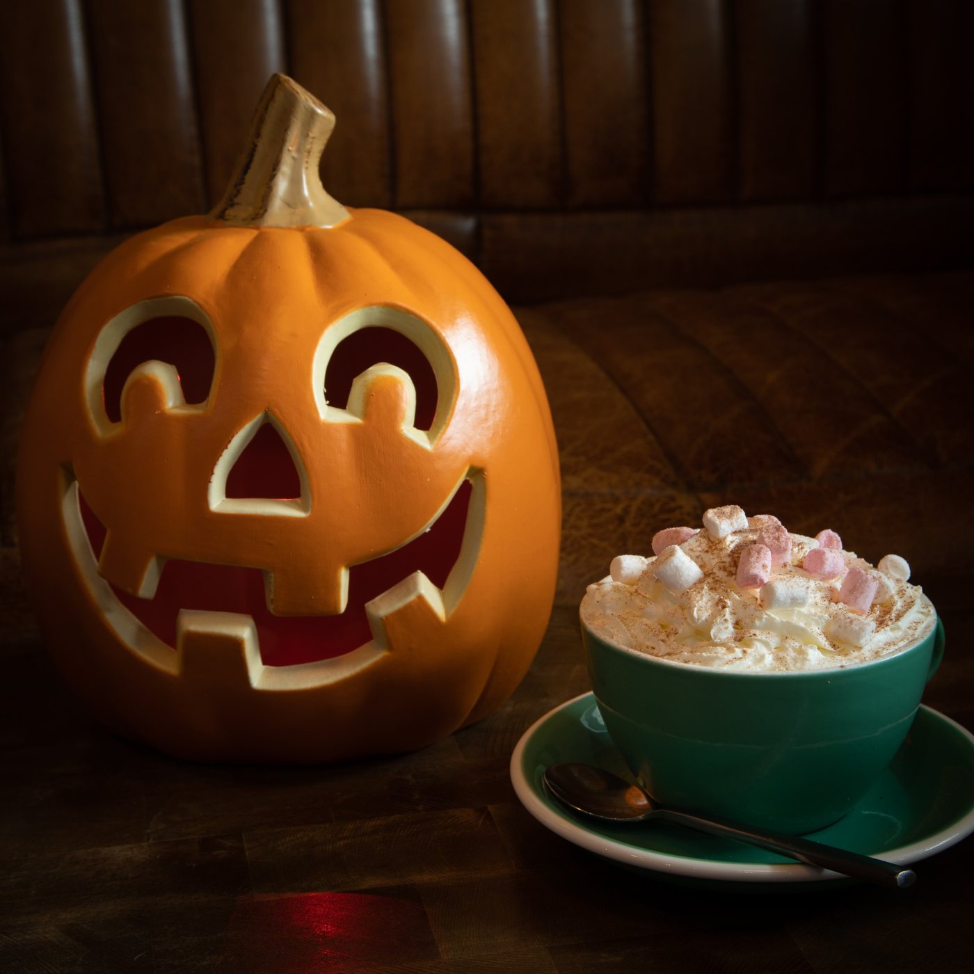 A carved pumpkin beside a hot chocolate piled with cream and marshmallows