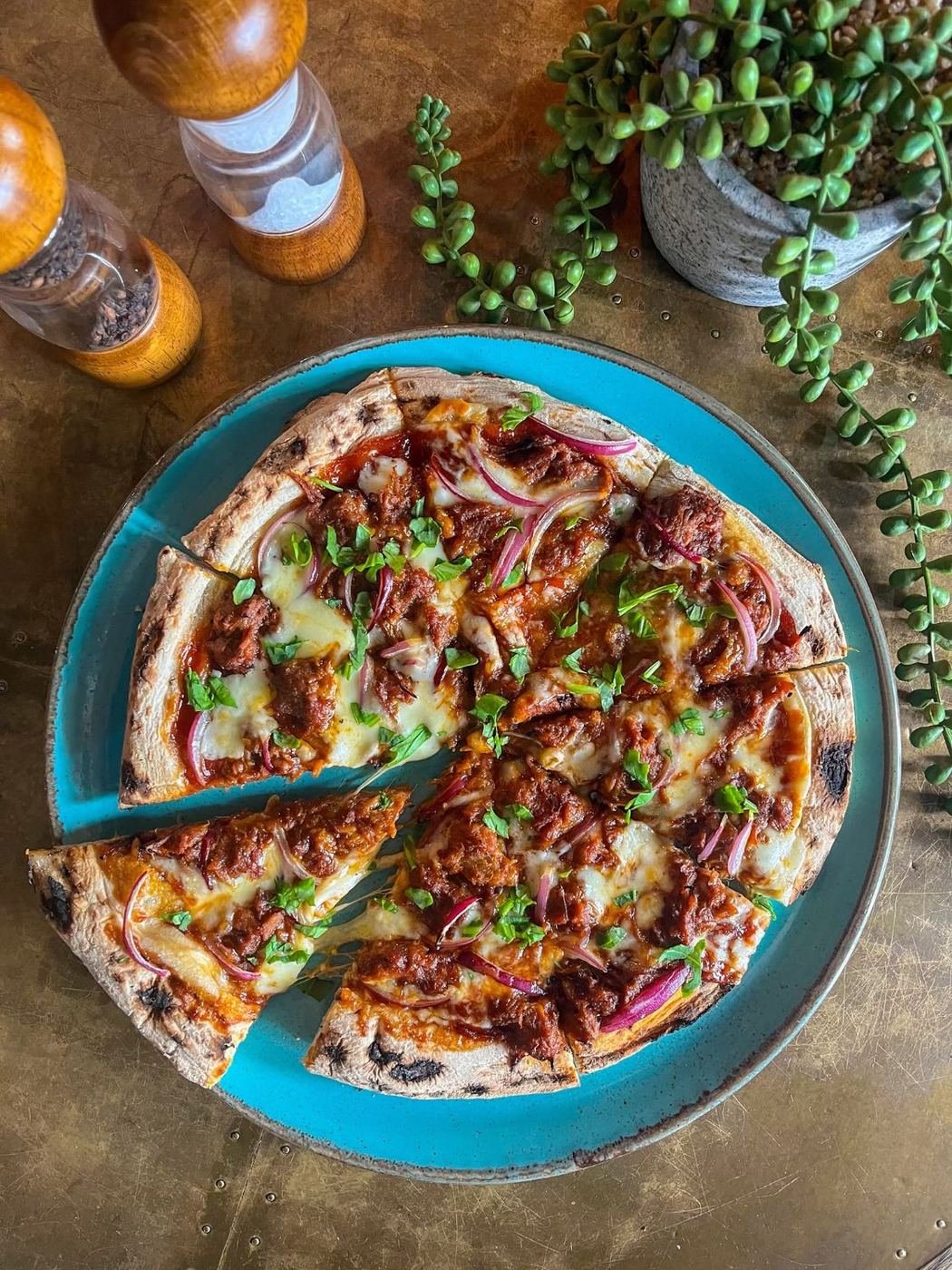 A barbecue pizza with red onion and fresh herbs, sliced on a blue plate